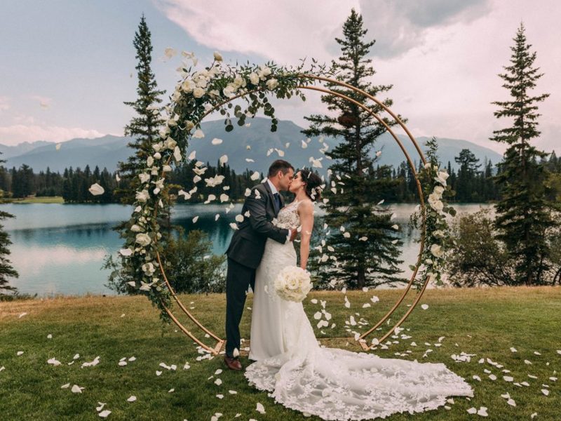 couple kissing in front of lake in Jasper with a shower of flower petals | Jasper Alberta wedding photographer
